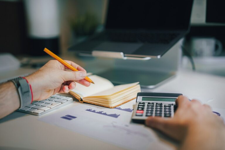 Calculator and notebook used to plan a 50/30/20 budget split into needs, wants, and savings